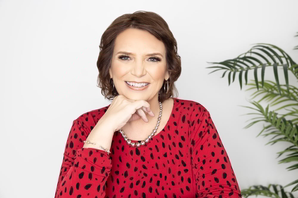 Denise Praul smiling confidently in a red patterned top, seated indoors; expert in referral marketing strategy.